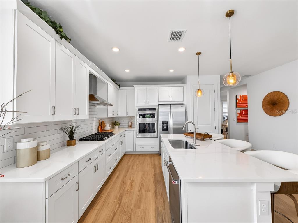 A modern white kitchen features a large island, stainless steel appliances, and wood-look flooring — 8841 OCEANA WAY, NAPLES, FL