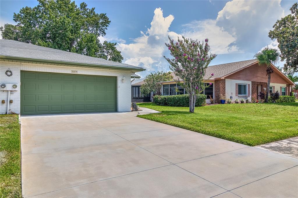 A concrete driveway leads to a house with a green garage door and white brick — 3217 MCMATH DRIVE, PALM HARBOR, FL