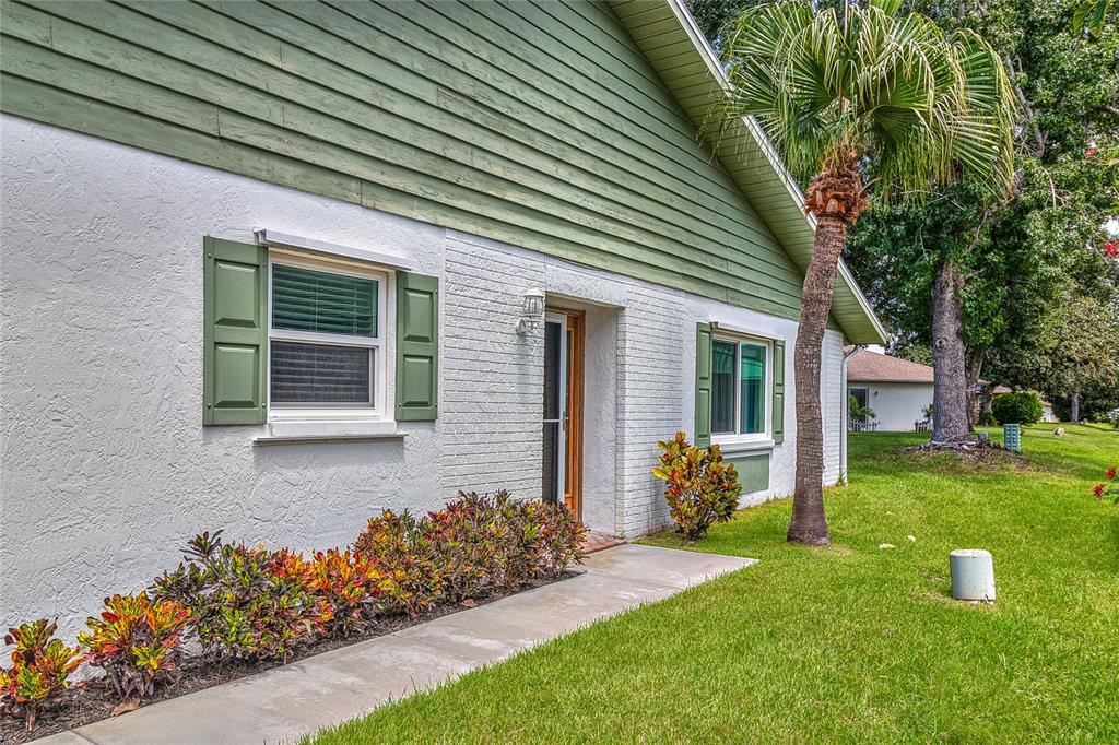 A single-story house exterior features white brick and stucco walls with green siding and shutters — 3217 MCMATH DRIVE, PALM HARBOR, FL