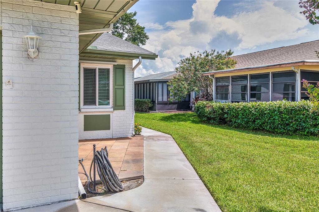 A white brick house exterior features a patio, a concrete walkway, and a green lawn — 3217 MCMATH DRIVE, PALM HARBOR, FL