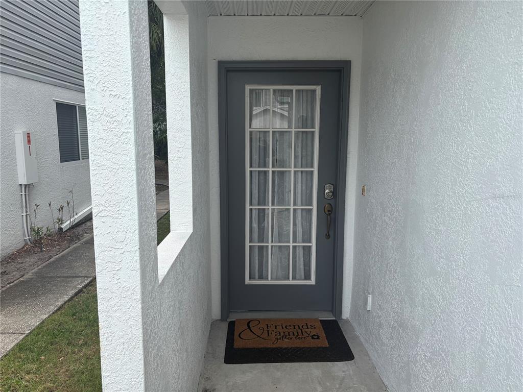 A gray front door with a glass pane sits under a covered entryway — 9122 JAKES PATH, LARGO, FL