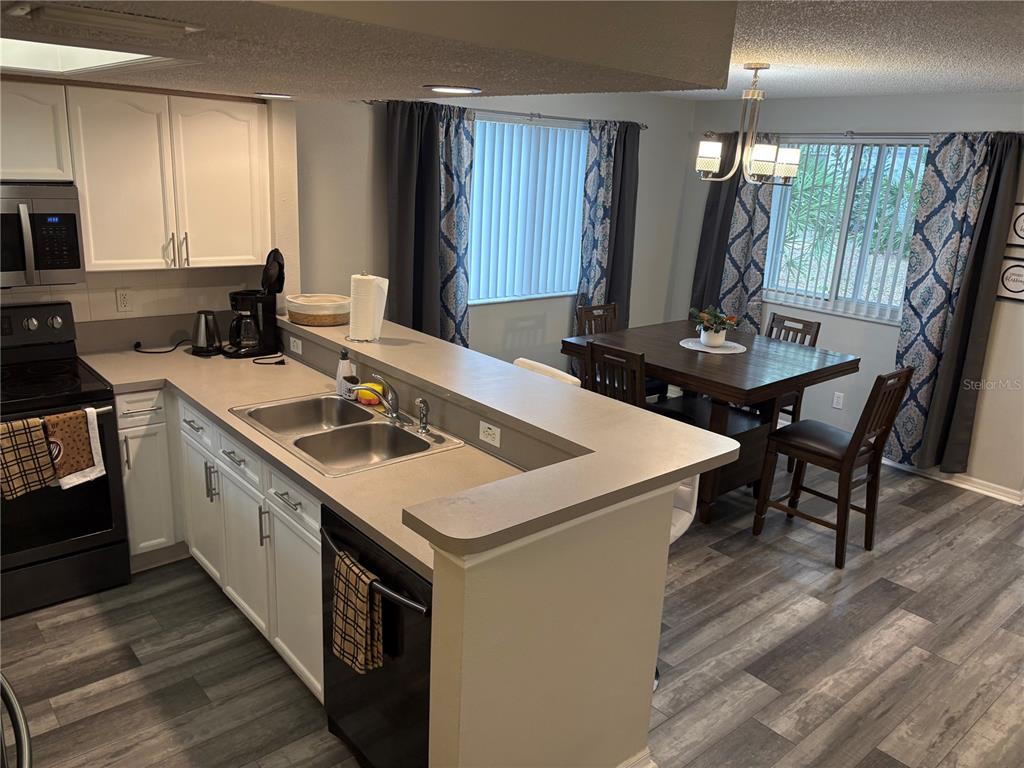 A kitchen with white cabinets and a breakfast bar overlooks a dining area with wood flooring — 9122 JAKES PATH, LARGO, FL