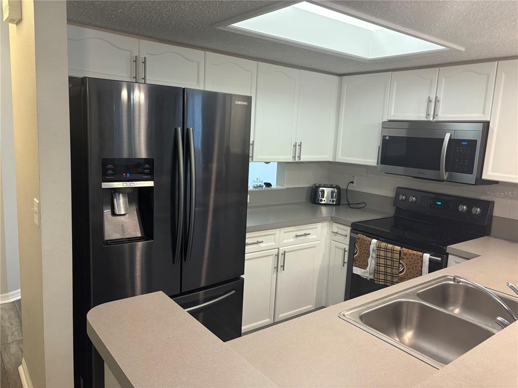A kitchen features white cabinets, gray countertops, and black stainless steel appliances — 9122 JAKES PATH, LARGO, FL