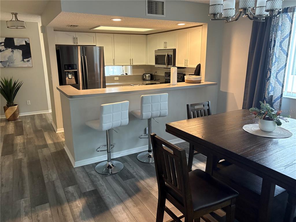 A kitchen with white cabinets and stainless steel appliances overlooks a dining area with wood flooring — 9122 JAKES PATH, LARGO, FL