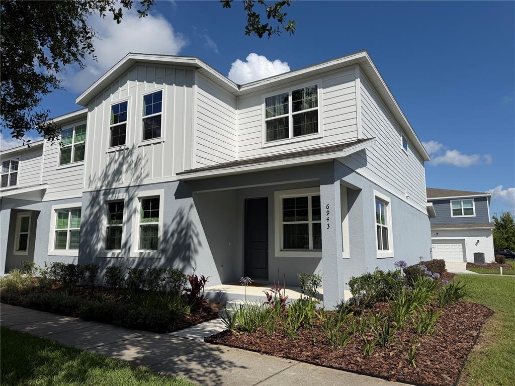 A two-story house with light gray and white siding features a covered front porch — 6943 FIVE OAKS DRIVE, HARMONY, FL