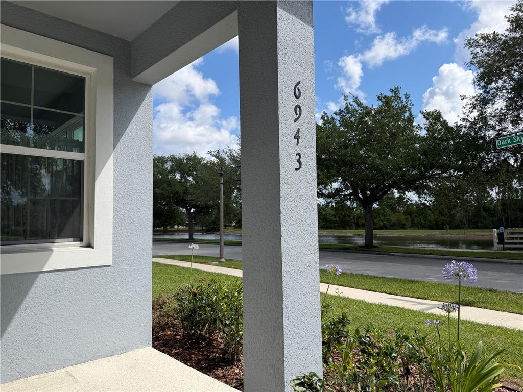 A vertical house number is mounted on a gray stucco porch pillar near a street — 6943 FIVE OAKS DRIVE, HARMONY, FL
