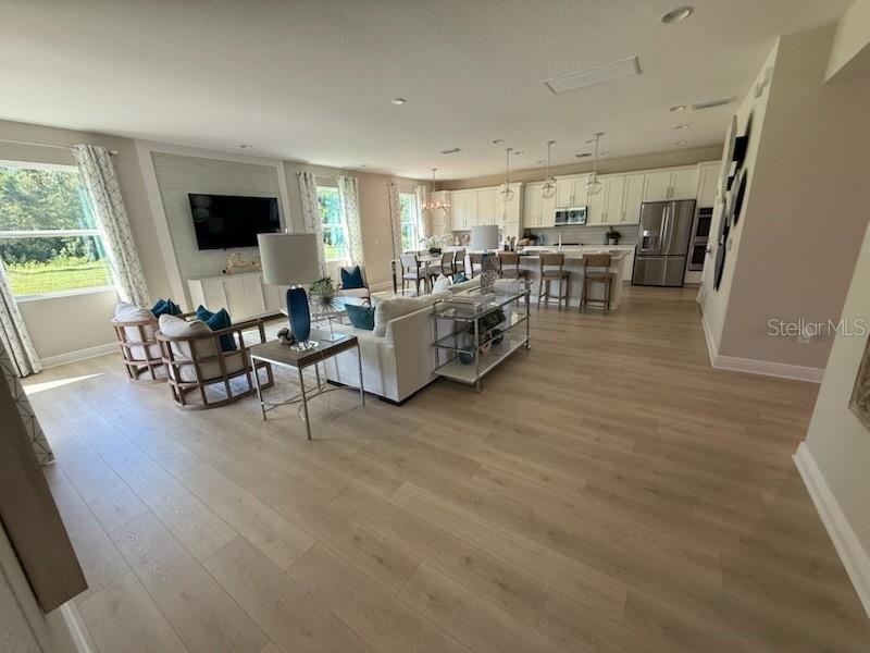 An open-concept living room and kitchen featuring light wood flooring and neutral-toned furniture — 5288 OBSIDIAN GATE DRIVE, MOUNT DORA, FL
