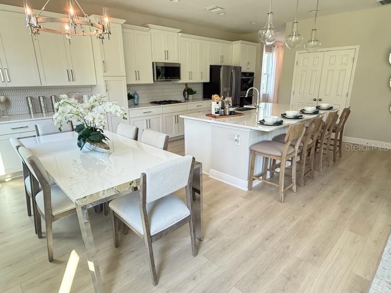 A bright kitchen features white cabinets, a large island with bar seating, and a dining area — 5288 OBSIDIAN GATE DRIVE, MOUNT DORA, FL