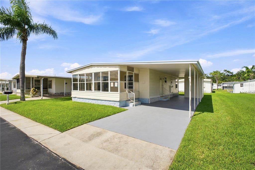 A single-story mobile home with a screened-in porch, carport, and lawn under a blue sky — 10913 JUSTICE DRIVE, PORT RICHEY, FL