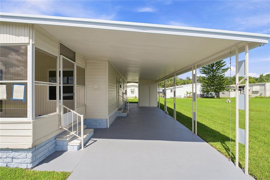 A mobile home exterior features a covered carport, a screened-in porch, and a concrete driveway — 10913 JUSTICE DRIVE, PORT RICHEY, FL