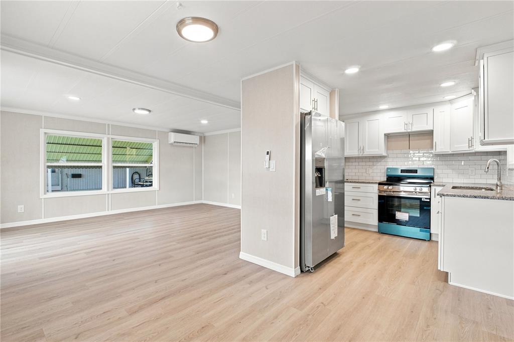 An open-concept kitchen and living area feature light wood flooring, white cabinets, and stainless appliances — 10913 JUSTICE DRIVE, PORT RICHEY, FL