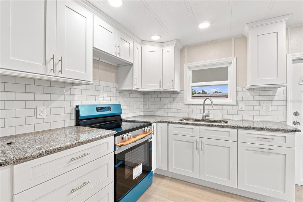 A kitchen featuring white cabinets, granite countertops, a subway tile backsplash, and a blue stove — 10913 JUSTICE DRIVE, PORT RICHEY, FL