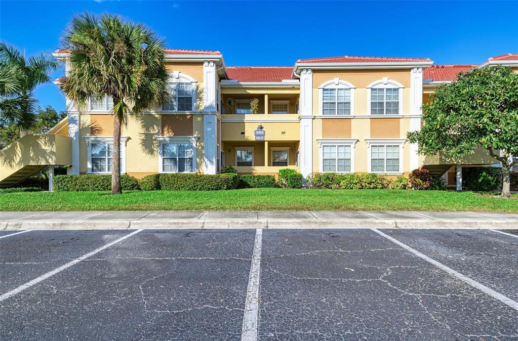 A two-story apartment building with a tiled roof, tan stucco walls, and a parking lot — 3005 CHIANTI COURT UNIT 1003, SARASOTA, FL
