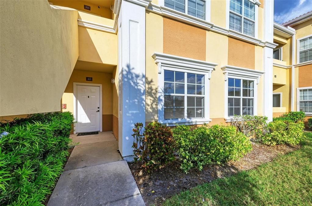 An exterior view of a yellow apartment building with a white door labeled 103 — 3005 CHIANTI COURT UNIT 1003, SARASOTA, FL
