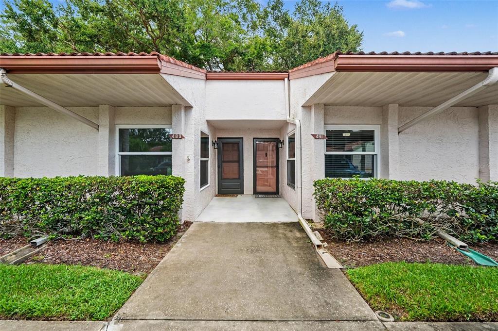 The exterior of a single-story duplex features two front doors, windows, and manicured hedges — 491 EXMOOR TERRACE, DUNEDIN, FL
