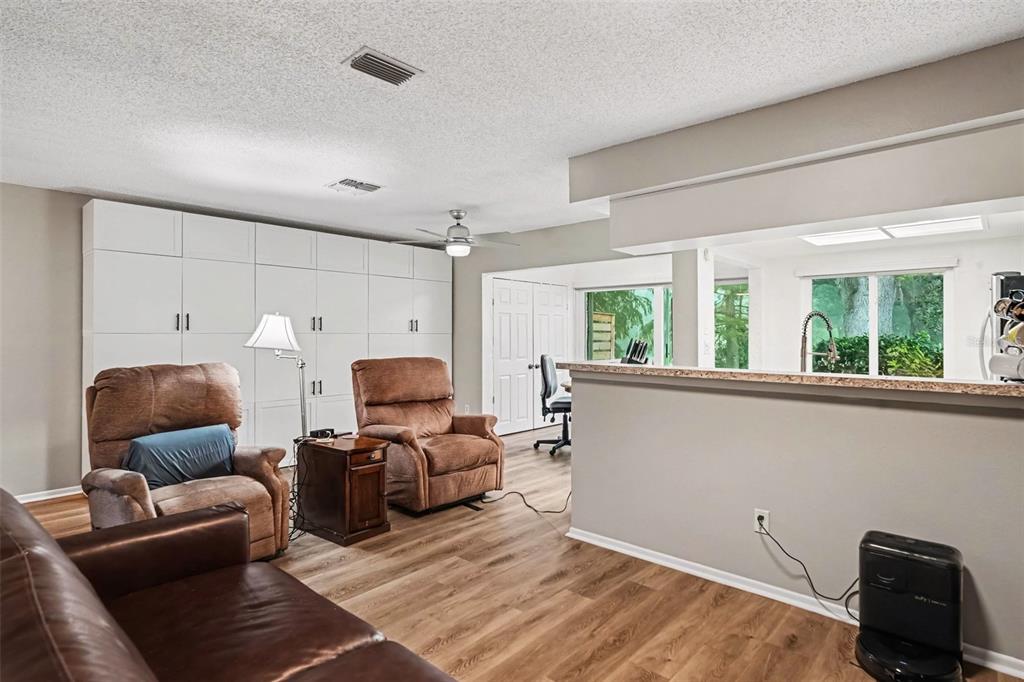 A living room with wood-look flooring, brown recliners, a leather sofa, and white built-in cabinets — 491 EXMOOR TERRACE, DUNEDIN, FL