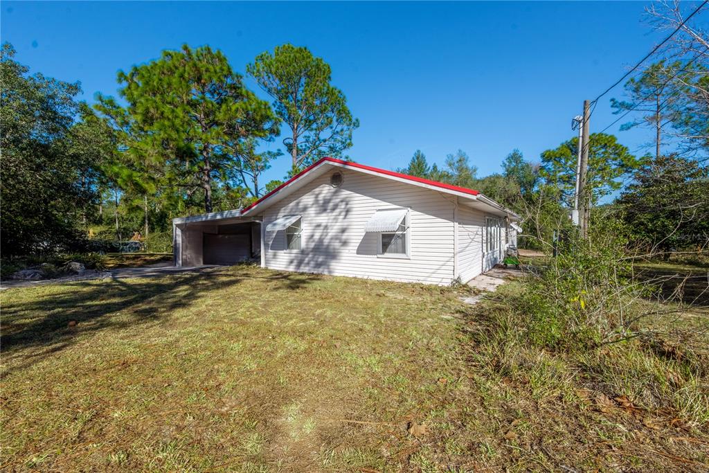 A white, single-story house with a red roof and an attached carport sits on grass — 11216 NE 63RD PLACE, WILLISTON, FL