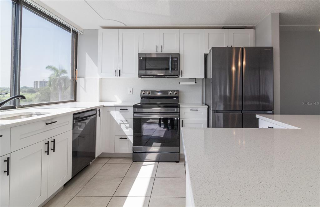 A kitchen features white cabinets, stainless steel appliances, quartz countertops, and a large window — 1500 PRESIDENTIAL WAY UNIT 401, WEST PALM BEACH, FL