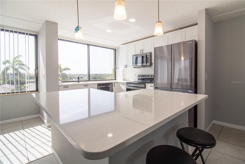A kitchen features white cabinetry, a quartz island, stainless steel appliances, and a large window — 1500 PRESIDENTIAL WAY UNIT 401, WEST PALM BEACH, FL