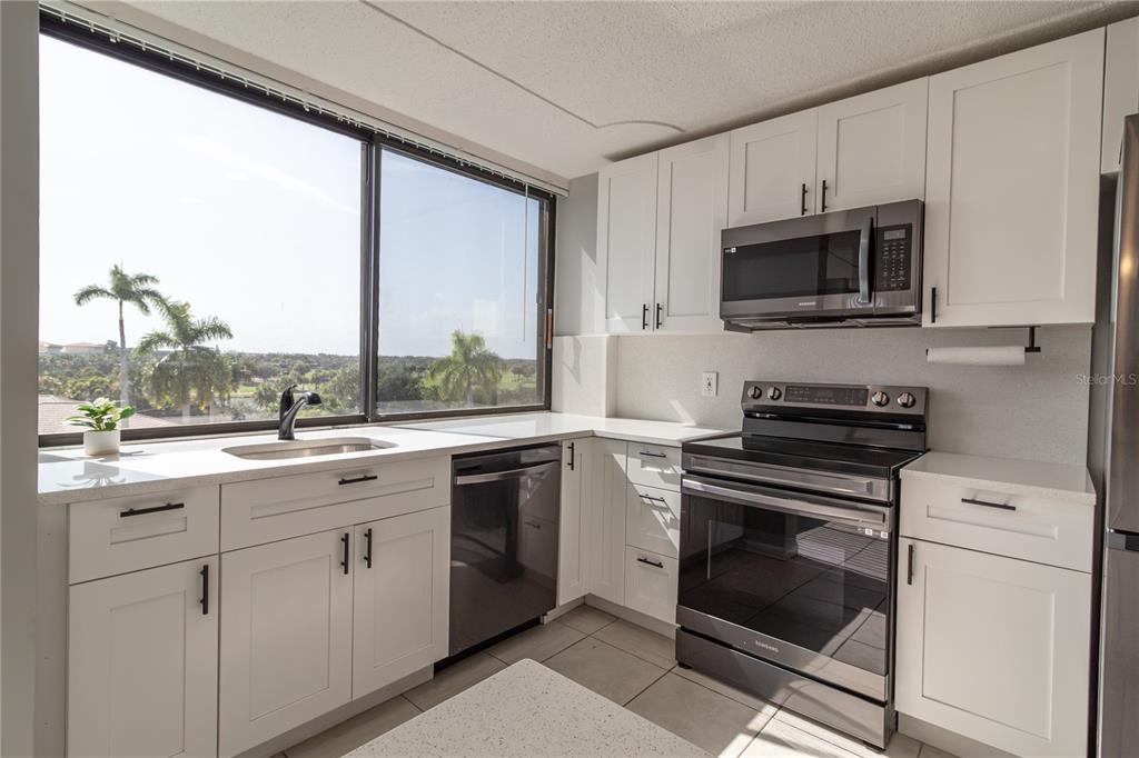 A modern kitchen features white cabinetry, stainless steel appliances, and a large window with palm trees — 1500 PRESIDENTIAL WAY UNIT 401, WEST PALM BEACH, FL