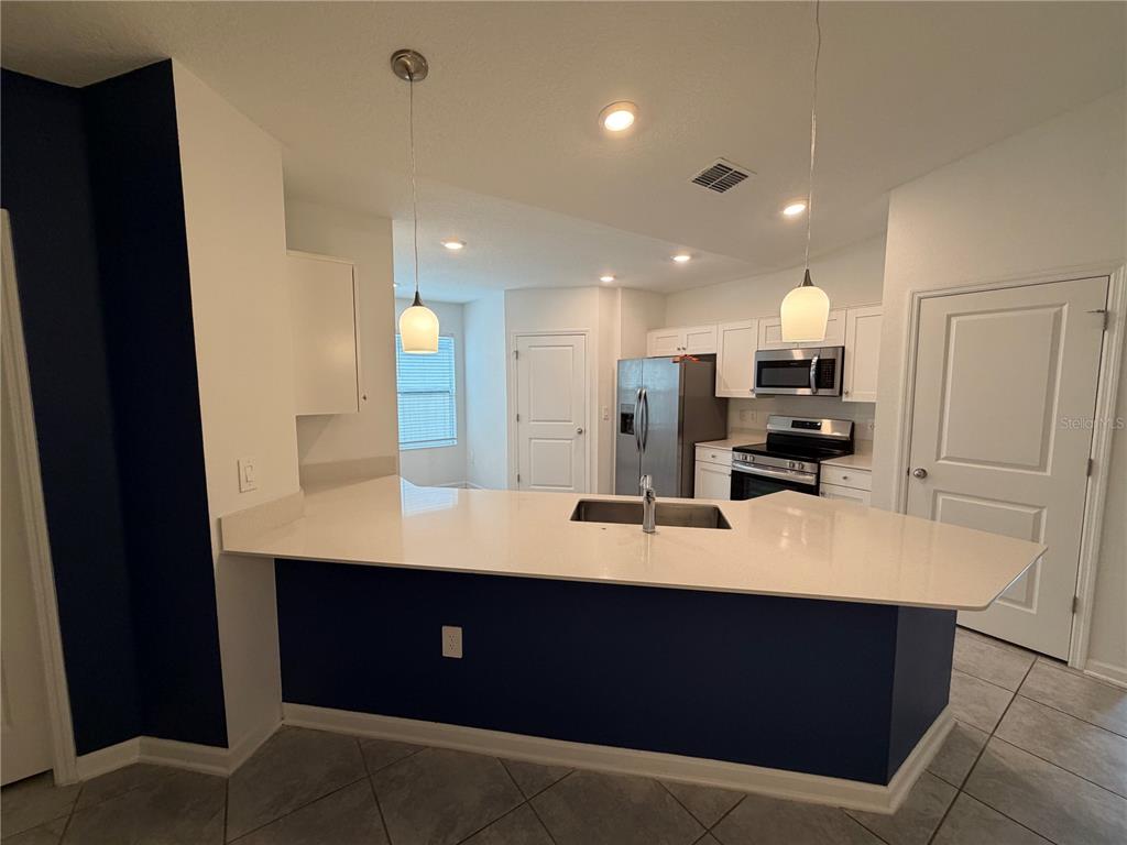 A kitchen with a white quartz island, bar seating, and tile flooring leads to a dining area — 225 LAWSON AVENUE, HAINES CITY, FL