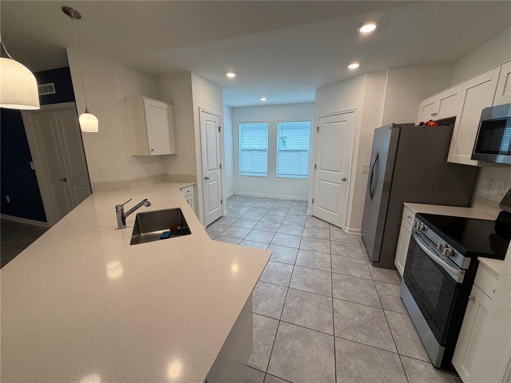 A kitchen features a dark blue island with white bar stools and stainless steel appliances — 225 LAWSON AVENUE, HAINES CITY, FL
