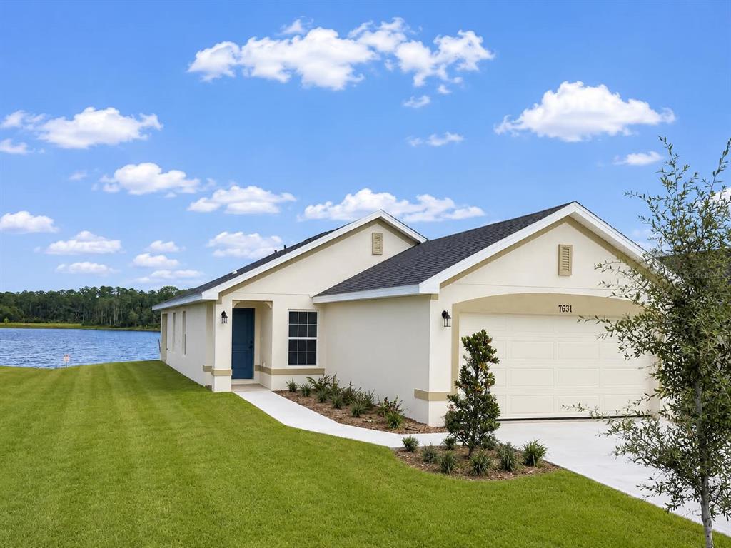 A single-story house with a white stucco exterior and a two-car garage beside a lake — 7631 BENT TREE LOOP, ST CLOUD, FL