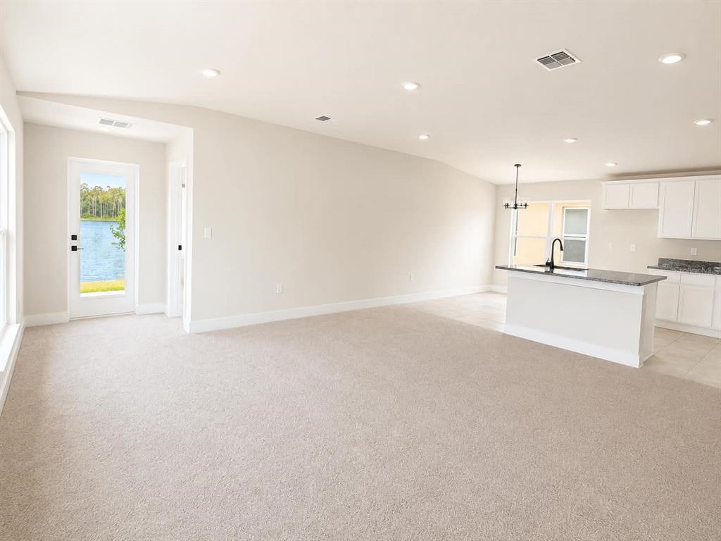 A carpeted living room opens to a kitchen with a white island and water view — 7631 BENT TREE LOOP, ST CLOUD, FL