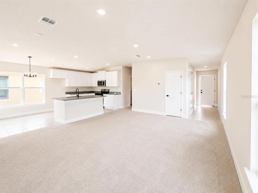 An open-concept living area features beige carpeting, a white kitchen with an island, and recessed lighting — 7631 BENT TREE LOOP, ST CLOUD, FL