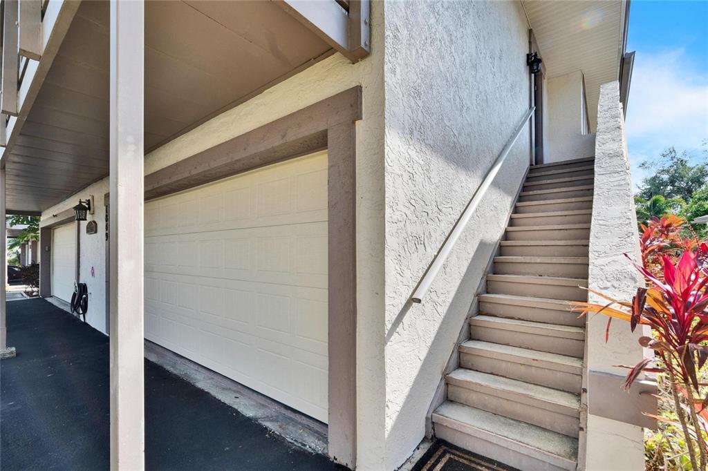 A white garage door sits beside an outdoor staircase leading to an upper-level entrance — 1849 BOUGH AVENUE UNIT D, CLEARWATER, FL