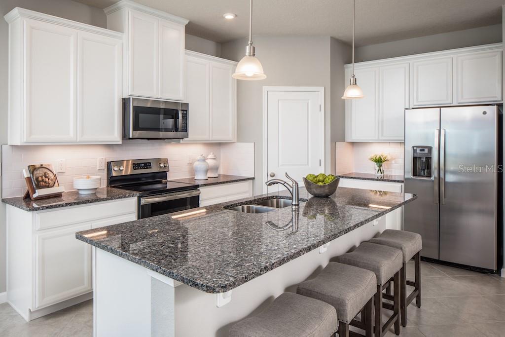 A kitchen features white cabinets, granite countertops, a center island with seating, and stainless appliances — 2578 WHITE LADYFISH ROAD, WIMAUMA, FL