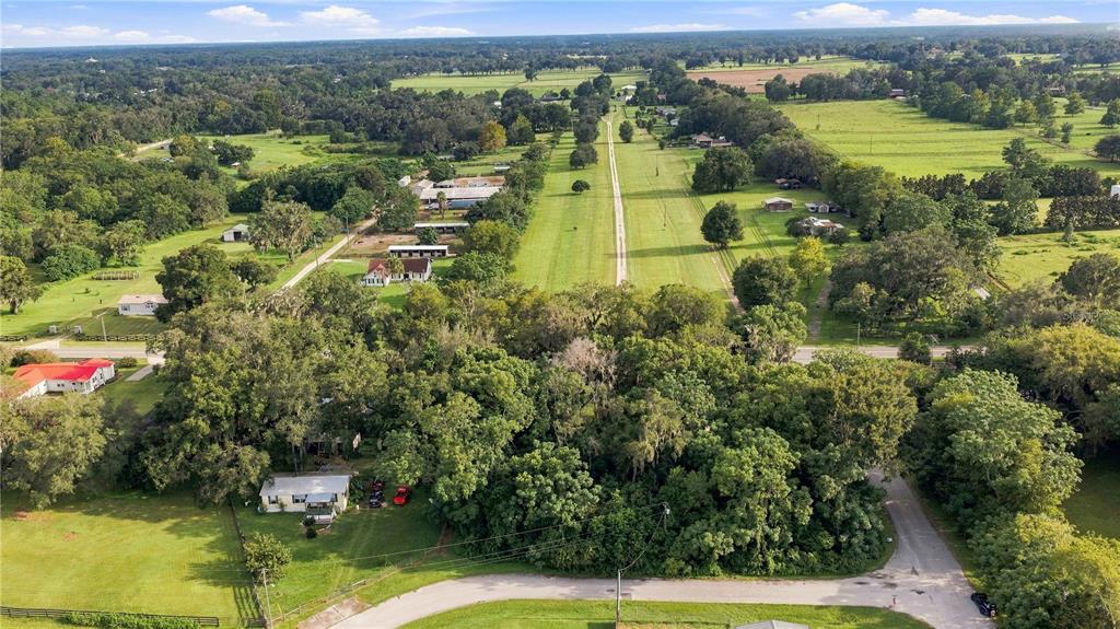 An aerial view shows a rural landscape with a long grass airstrip and scattered houses — 5860 SE 144TH PLACE, SUMMERFIELD, FL
