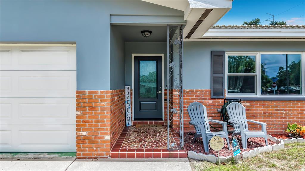 The exterior of a house features a brick facade, a dark front door, and two chairs — 2198 ACADEMY DRIVE, CLEARWATER, FL