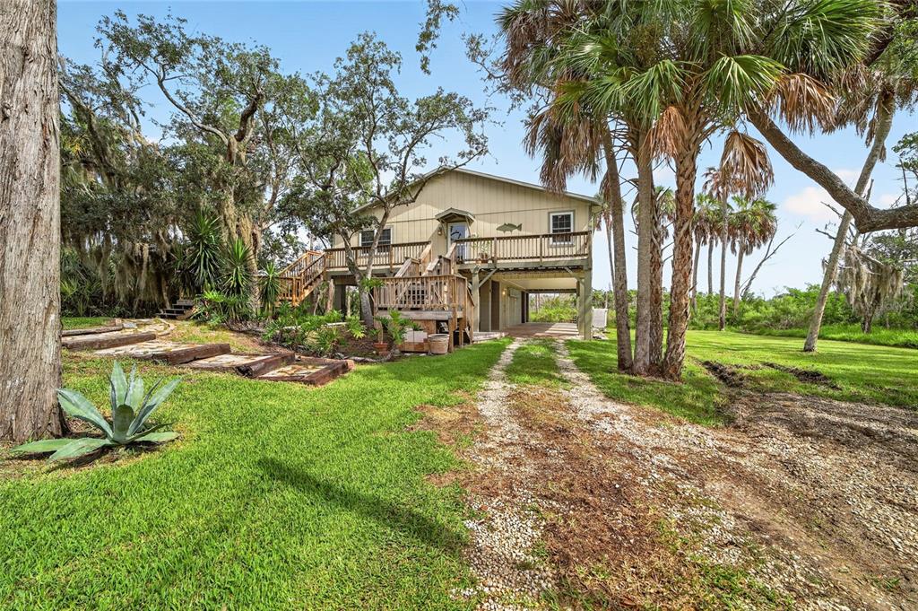 A two-story stilt house with a wooden deck and gravel driveway surrounded by palm trees — 14141 W BOARDWALK LANE, CRYSTAL RIVER, FL