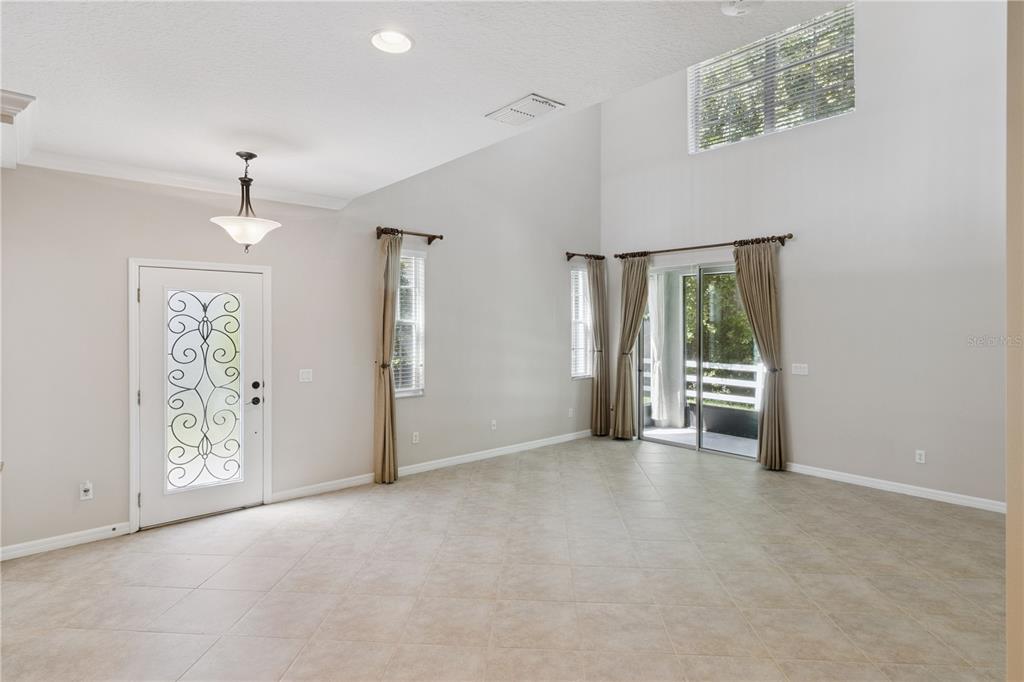An empty living room features high vaulted ceilings, tile flooring, a glass-paneled door, and sliding doors — 624 VENICE PLACE, SANFORD, FL