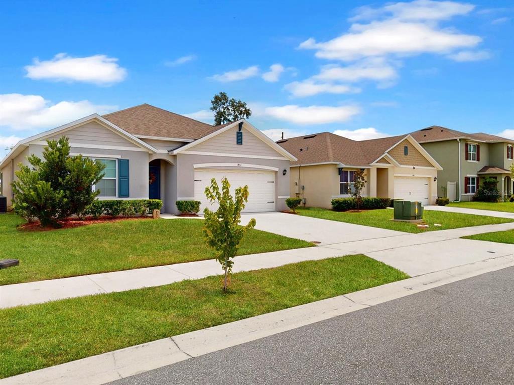 A street-level view of three suburban single-family homes with driveways and manicured lawns — 1451 OLIVE COURT, ST CLOUD, FL