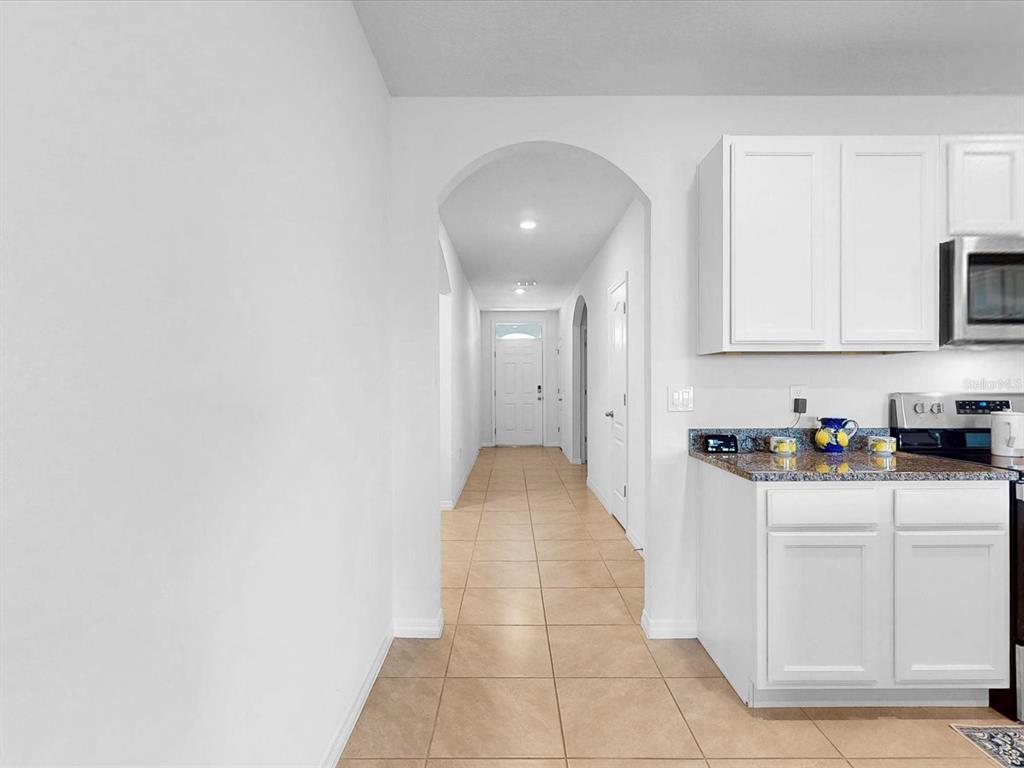 A kitchen with white cabinets and granite countertops opens into a hallway with tiled floors — 1451 OLIVE COURT, ST CLOUD, FL
