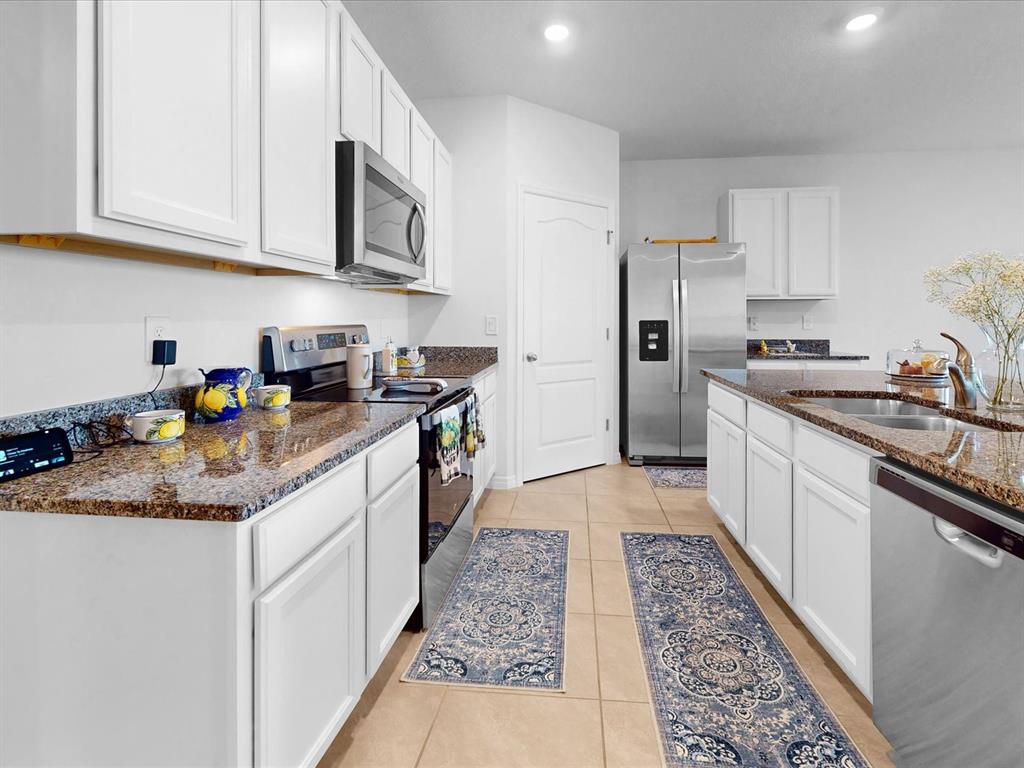 A kitchen with white cabinets, granite countertops, stainless steel appliances, and two blue runner rugs — 1451 OLIVE COURT, ST CLOUD, FL