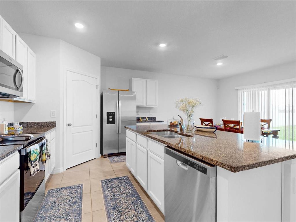 A kitchen features white cabinets, granite countertops, stainless steel appliances, and a central island — 1451 OLIVE COURT, ST CLOUD, FL