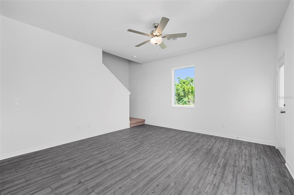 An empty room with gray wood-look flooring, white walls, a ceiling fan, and stairs — 564 BAY LEAF DRIVE, POINCIANA, FL