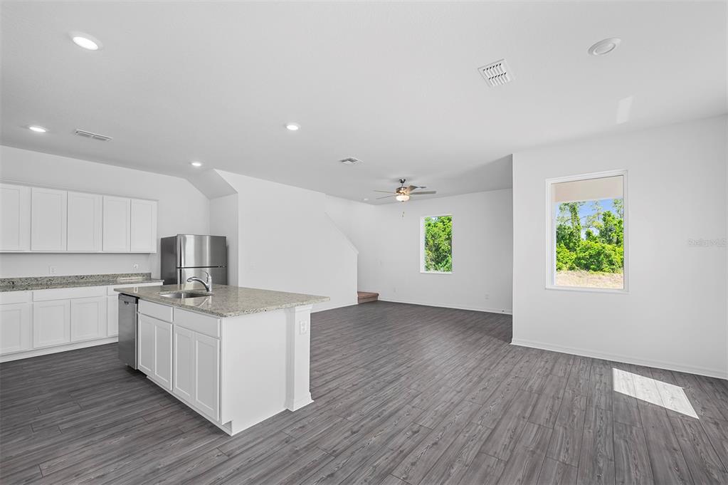 A kitchen with white cabinets and a granite island opens into a spacious living area — 564 BAY LEAF DRIVE, POINCIANA, FL