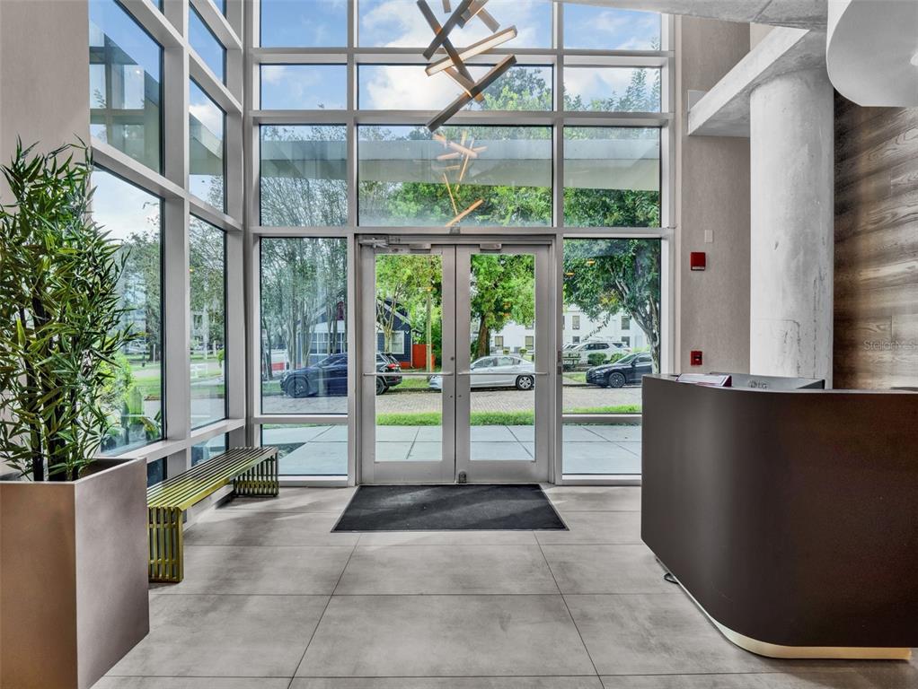 A modern building lobby features floor-to-ceiling windows, a reception desk, and a metal bench — 525 E JACKSON STREET UNIT 305, ORLANDO, FL