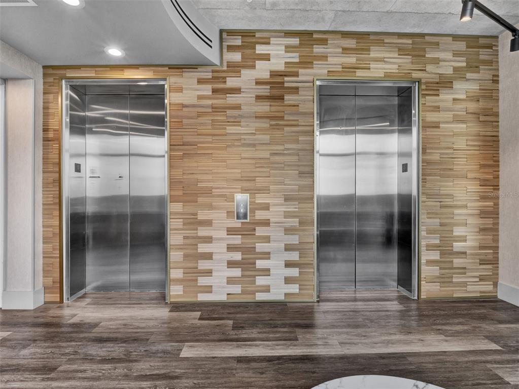 Two stainless steel elevators are set into a wall with textured, multi-toned wood paneling — 525 E JACKSON STREET UNIT 305, ORLANDO, FL