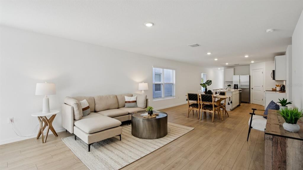 An open-concept living and dining area features light wood flooring, a sectional sofa, and kitchen — 17797 MOUNT BLACKBURN LANE, SPRING HILL, FL