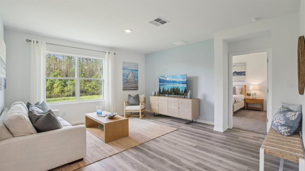 A living room features light wood flooring, a white sofa, and a view of trees — 15013 CROSSHALL STREAM DRIVE, WIMAUMA, FL
