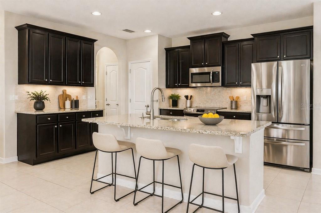 A kitchen features dark wood cabinets, granite countertops, stainless steel appliances, and three bar stools — 1501 PRAIRIE OAKS DRIVE, ST CLOUD, FL