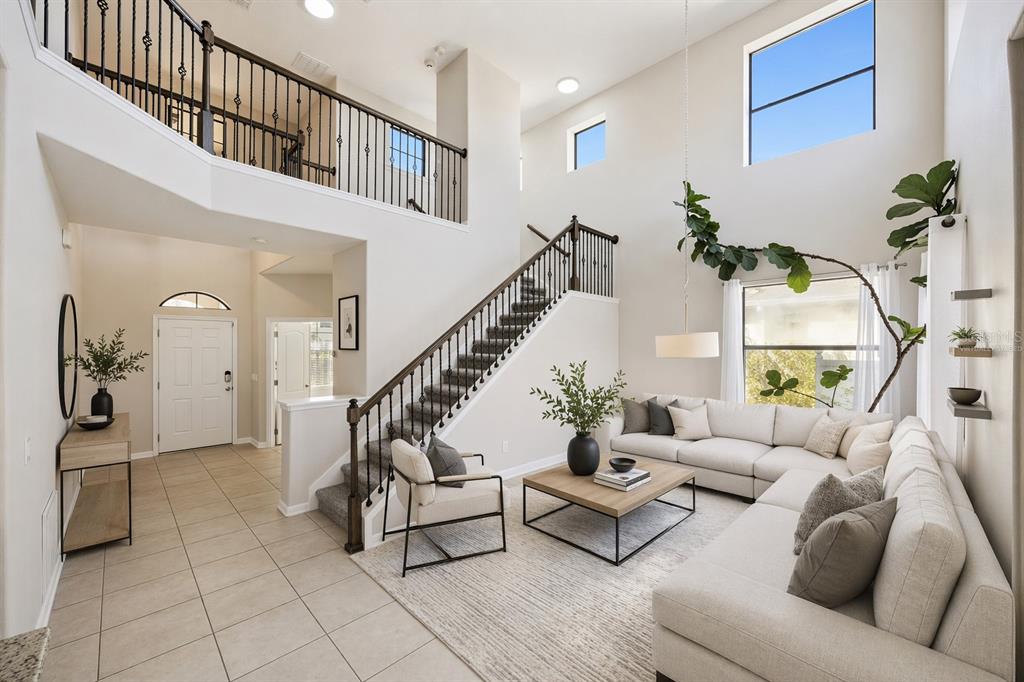 A high-ceilinged living room features a staircase, tile flooring, and a large sectional sofa — 1501 PRAIRIE OAKS DRIVE, ST CLOUD, FL