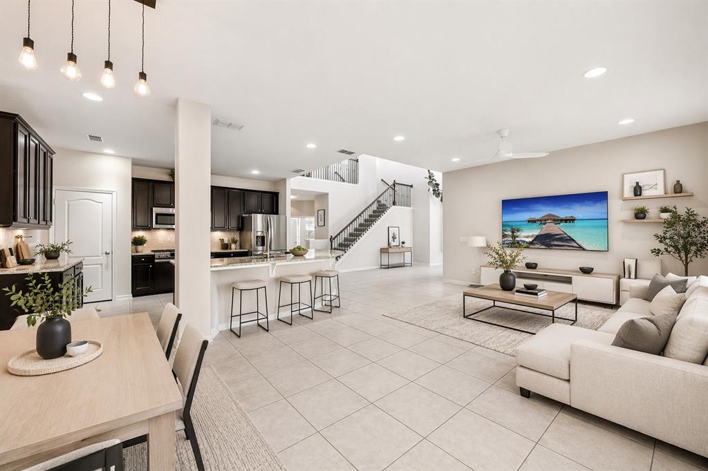 An open-concept living area features a kitchen with dark cabinets, a dining table, and stairs — 1501 PRAIRIE OAKS DRIVE, ST CLOUD, FL