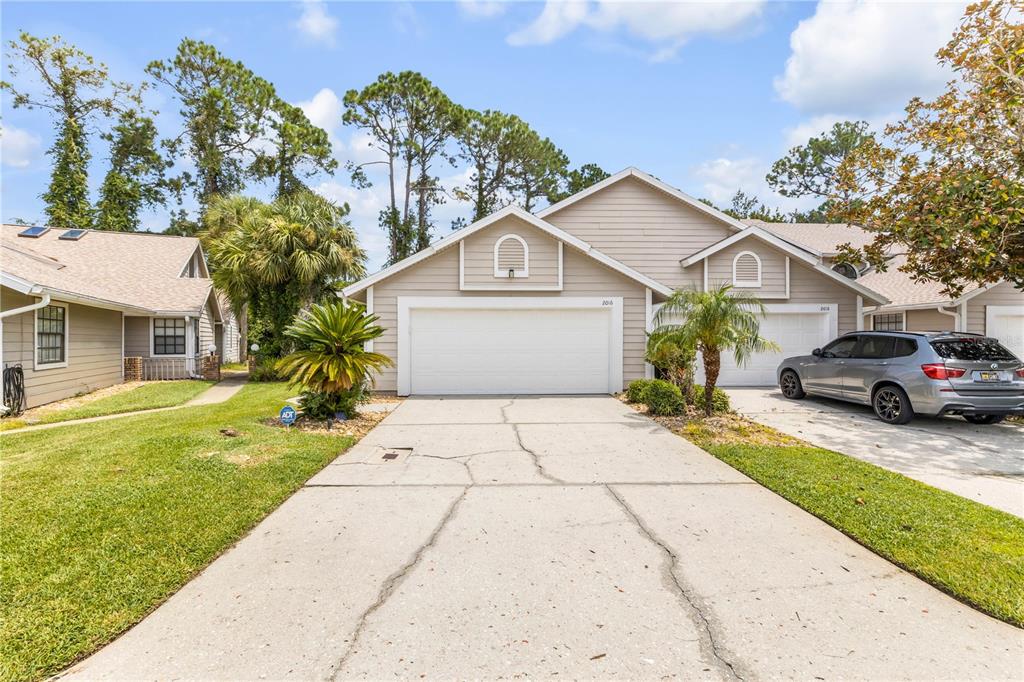 A beige single-story duplex with a shared concrete driveway and two white garage doors — 2016 CORNELL PLACE, PORT ORANGE, FL