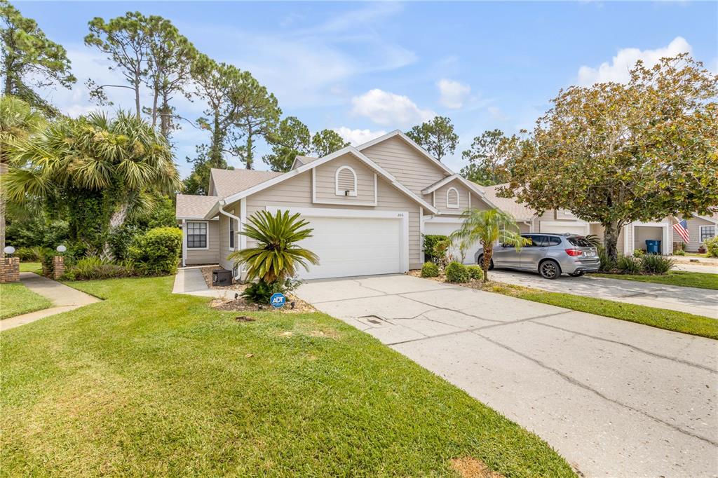 A beige, single-story house with a two-car garage, a concrete driveway, and surrounding landscaping — 2016 CORNELL PLACE, PORT ORANGE, FL